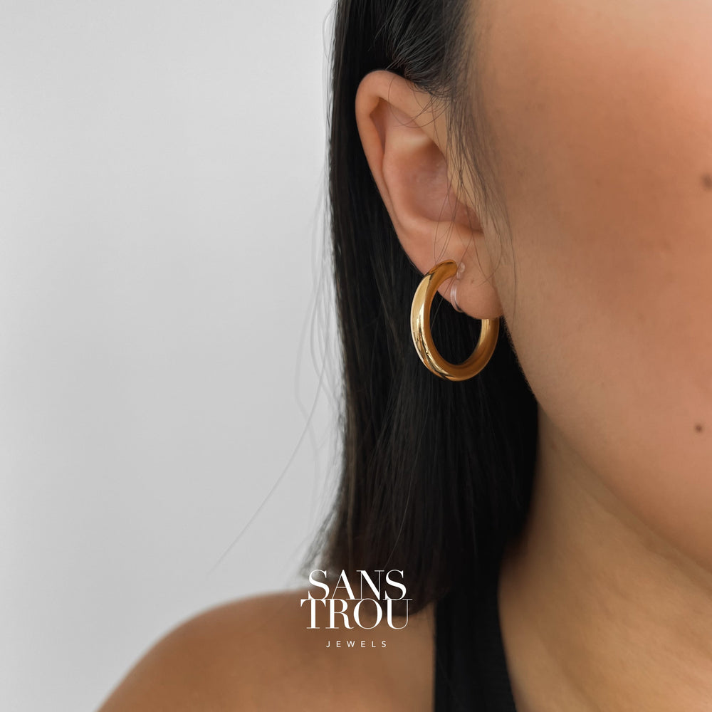 Model wearing classic gold clip-on hoops plated with 18k gold.  