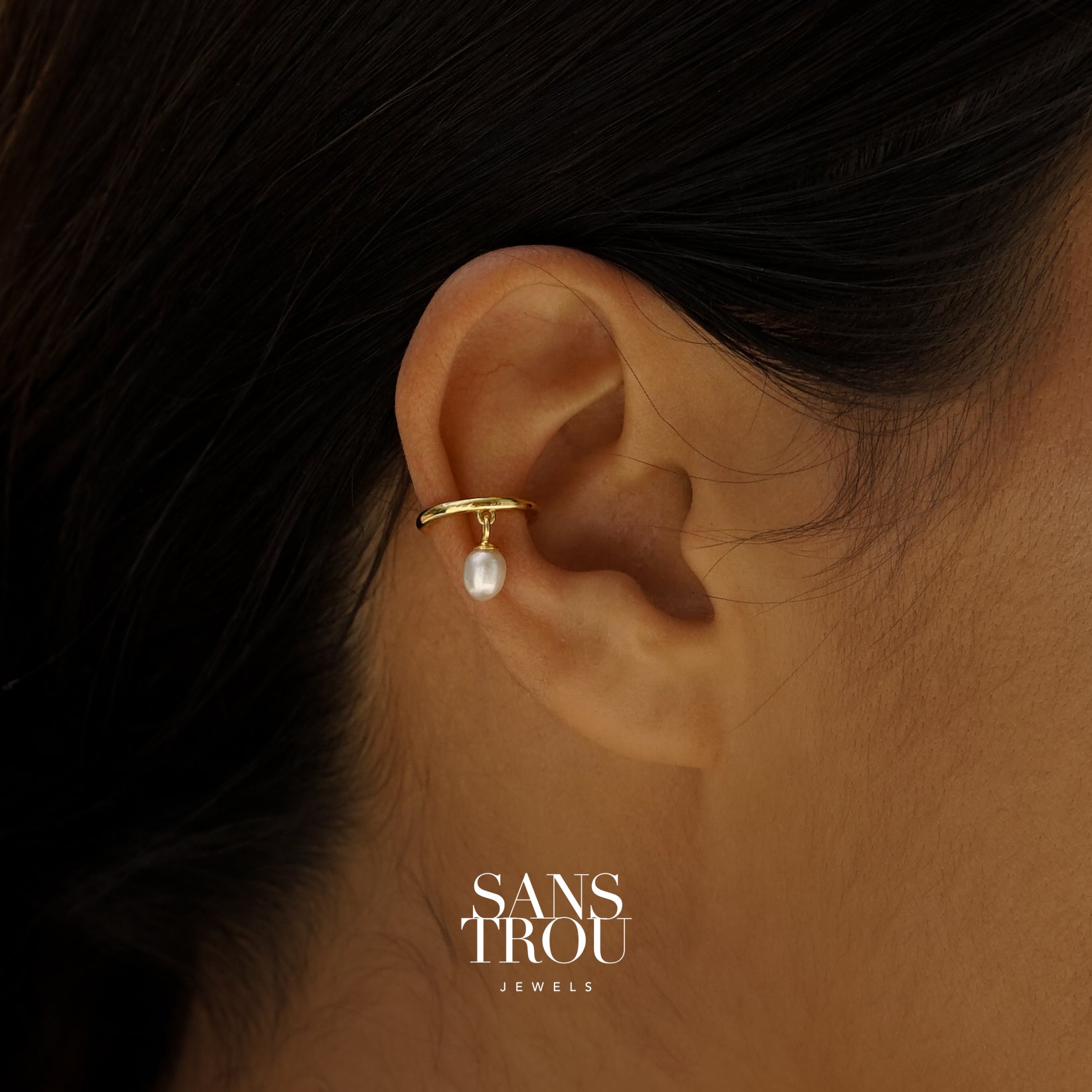 Close up of an ear cuff with dainty dangle freshwater pearl worn on an ear. Branded SANS TROU