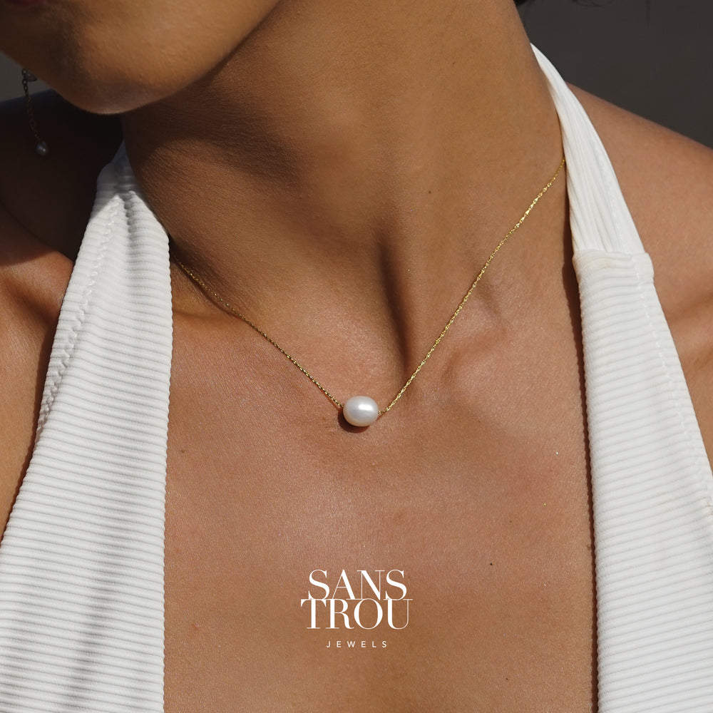 Dainty floating pearl necklace on a shiny gold chain, worn on a person
