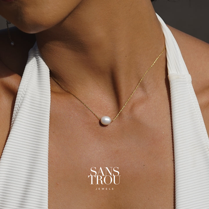 Dainty floating pearl necklace on a shiny gold chain, worn on a person