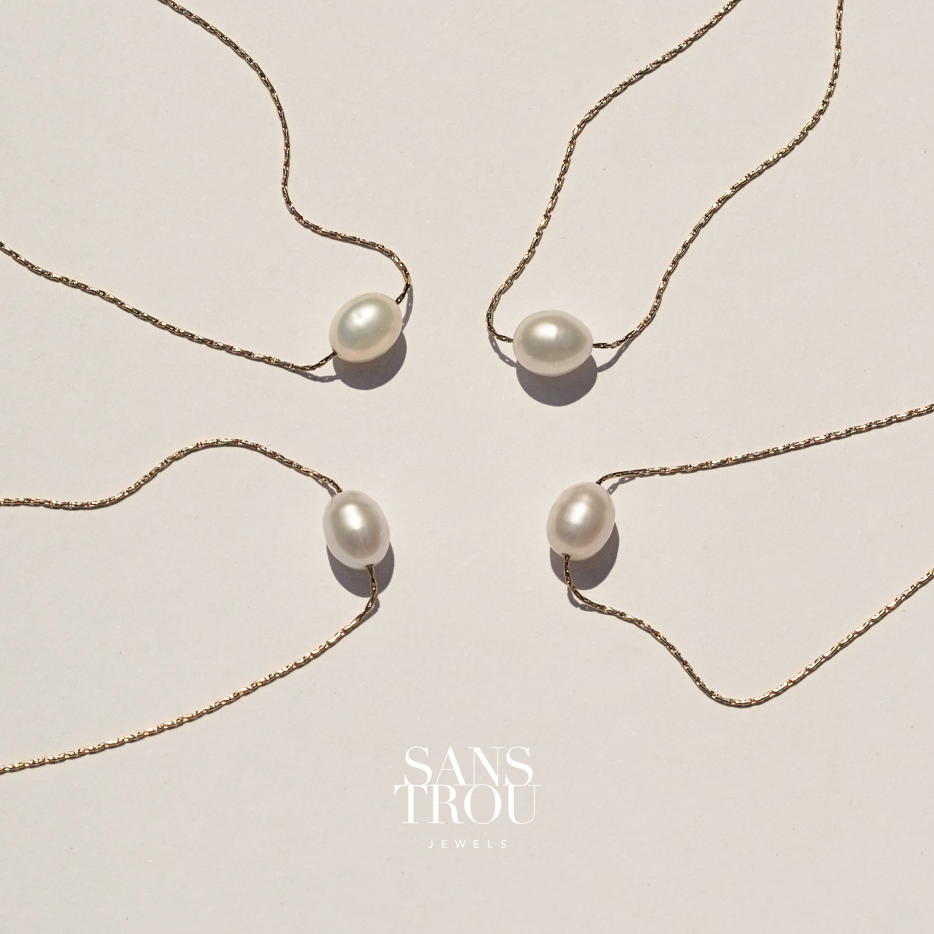 Dainty floating pearl necklace on a shiny gold chain, on a cream background