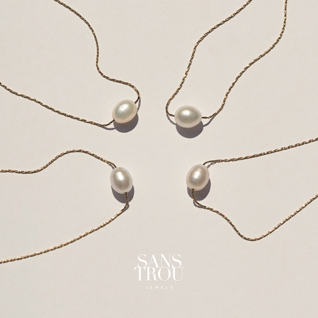 Dainty floating pearl necklace on a shiny gold chain, on a cream background