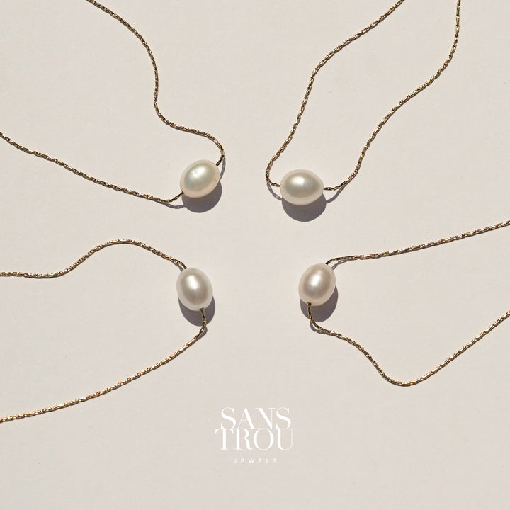 Dainty floating pearl necklace on a shiny gold chain, on a cream background