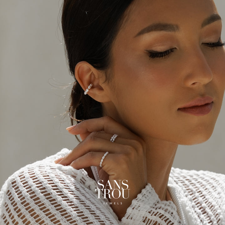 Close-up of a woman wearing pearl ear cuff and pearl rings 