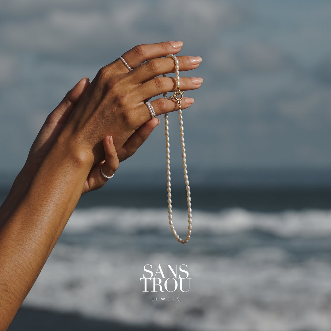 Hand holding a pearl necklace with ocean background