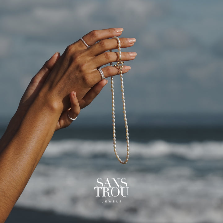 Hand holding a pearl necklace with ocean background