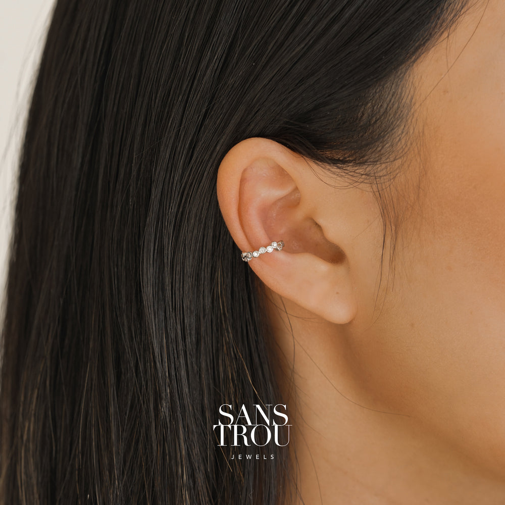 Model wearing a sterling silver ear cuff with CZ stones arranged in an asymmetrical composition. Model wears the cuff on the conch.