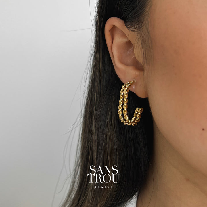 Gold clip-on earrings worn on model from front angle. Earrings feature two twisted rope bars that come together in a half hoop shape