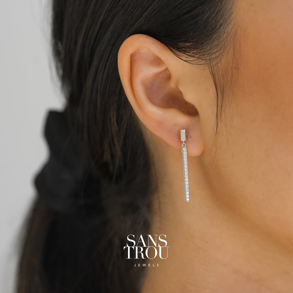 Model wears sterling silver clip-on drop earrings featuring a slim bar with CZ stones.