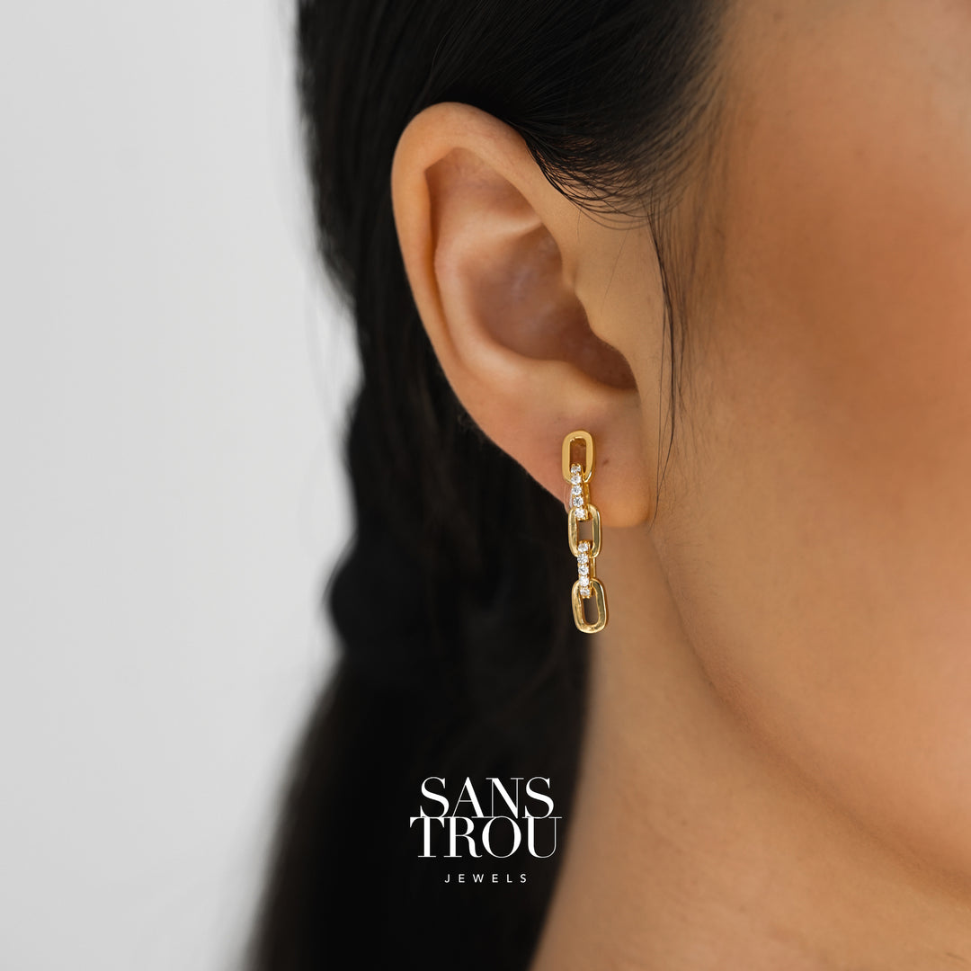 Model wears a gold three sequence chain drop-clip on earring. The earring is worn on the lobe and features CZ stones. 