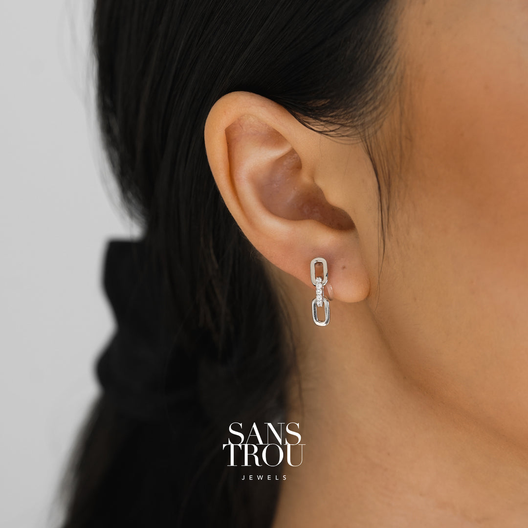 Model wears a dainty silver two sequence chain drop-clip on earring. The earring is worn on the lobe and features CZ stones. 