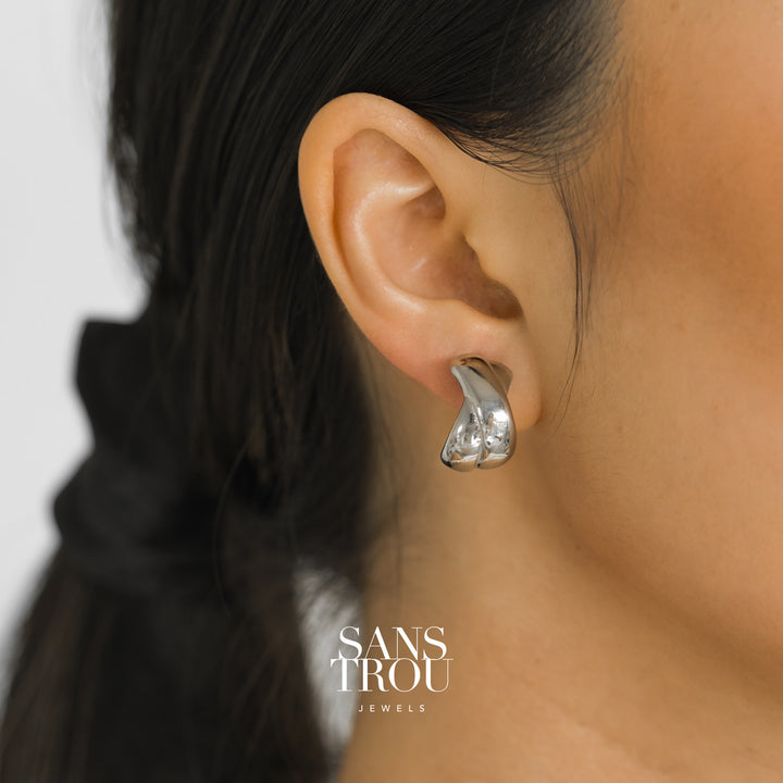 Model wears silver chunky criss cross clip-on earring on the lobe. The earring is attached with a hidden resin clip. 