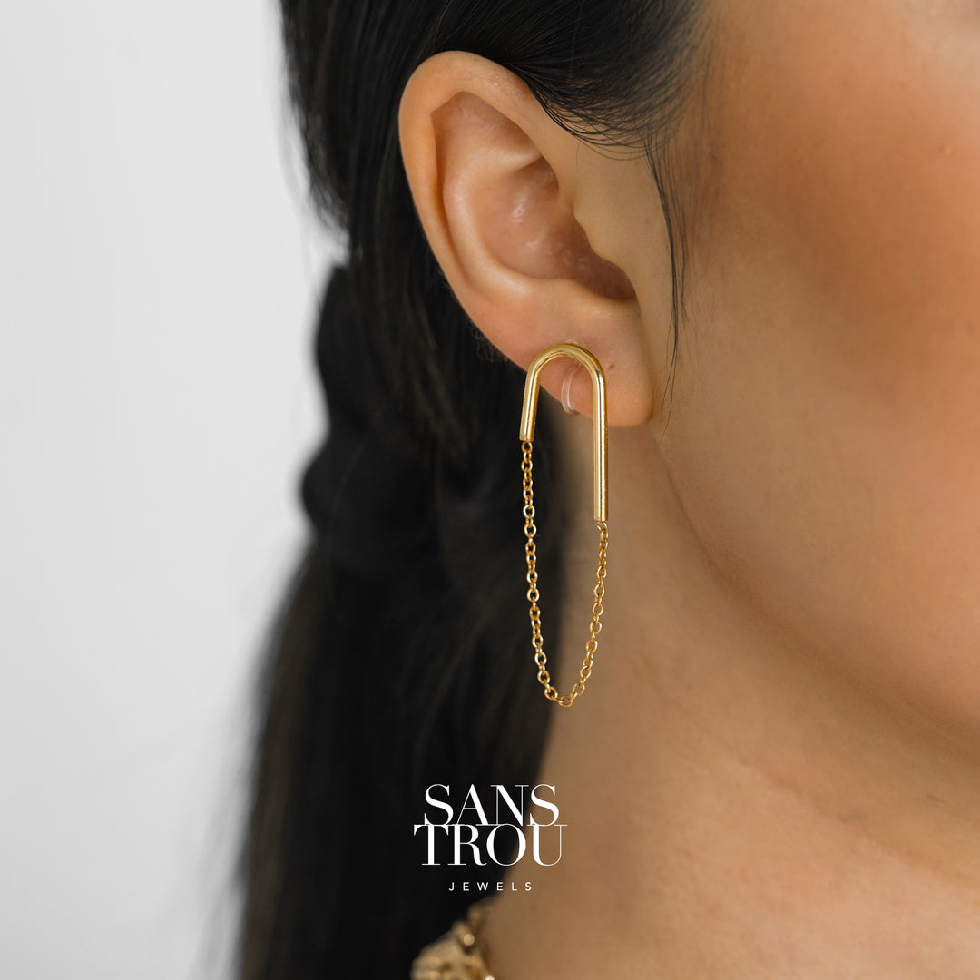 Model wears a gold U shaped clip-on earring with an attached drop chain. The Lea is worn on the lobe and has an asymmetrical pair. 