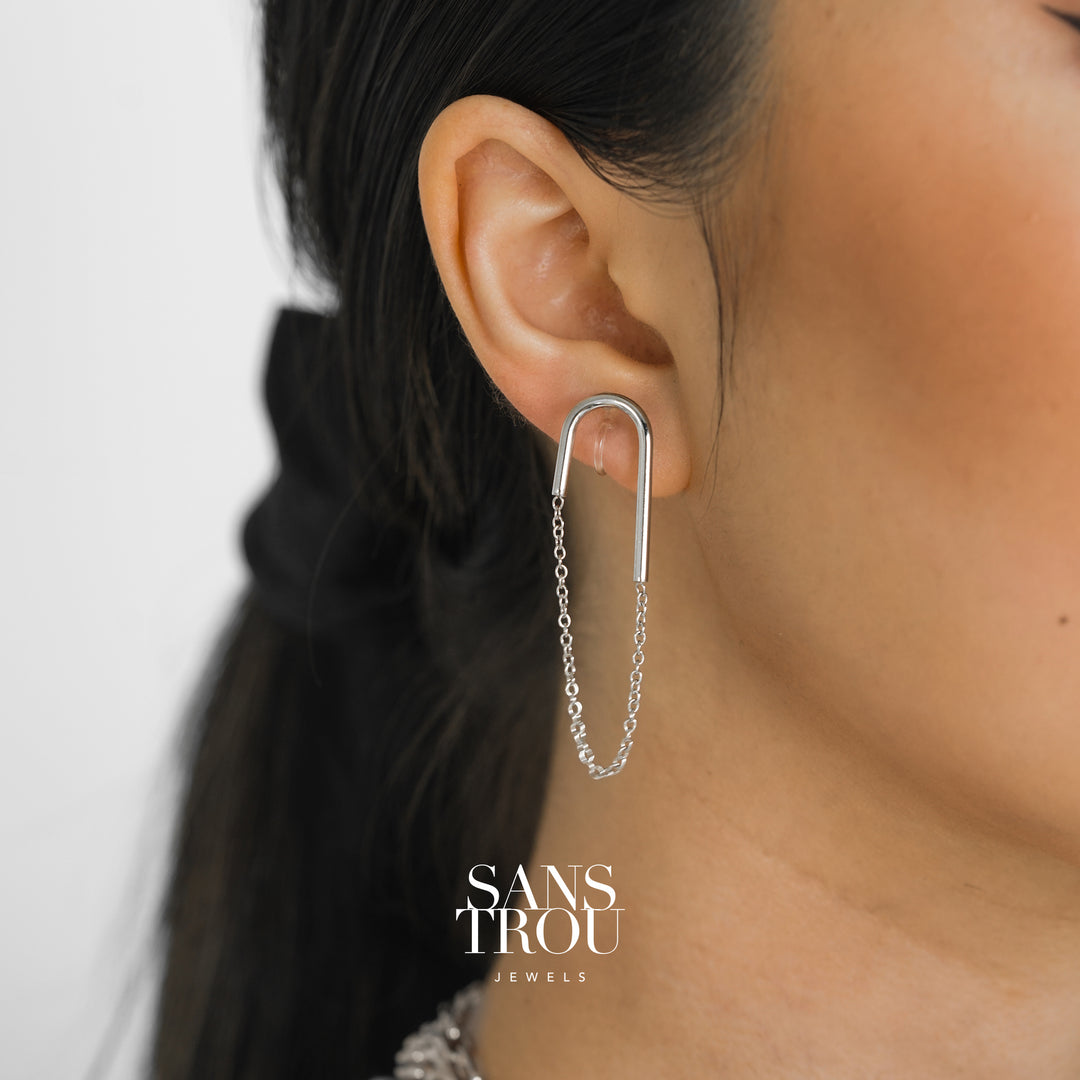 Model wears a silver U shaped clip-on earring with an attached drop chain. The Lea is worn on the lobe and has an asymmetrical pair. 