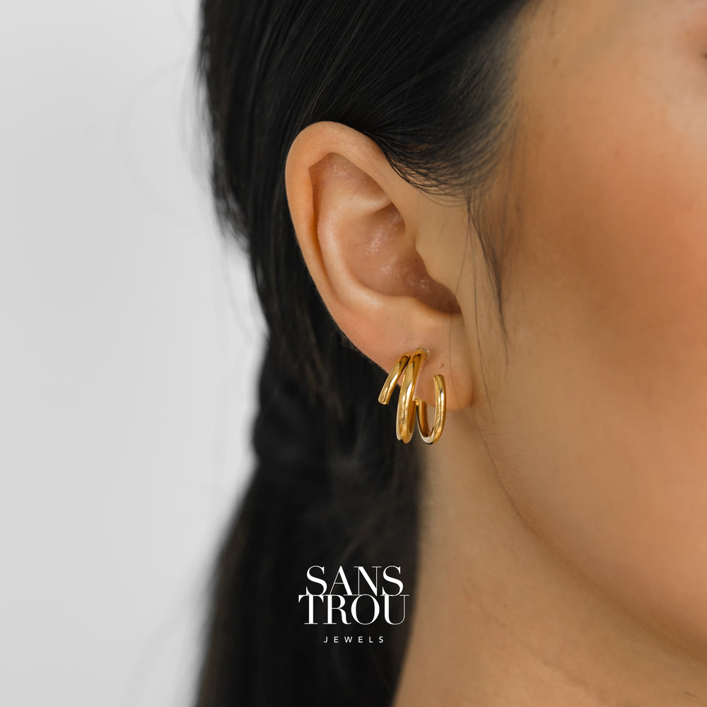 Model wears a pair of gold asymmetrical spiral clip-on earrings on the lobe. 