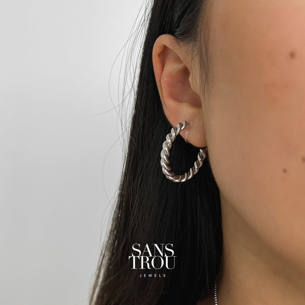 Model wears a twisted stainless steel plated clip-on hoop earring on the lobe. 