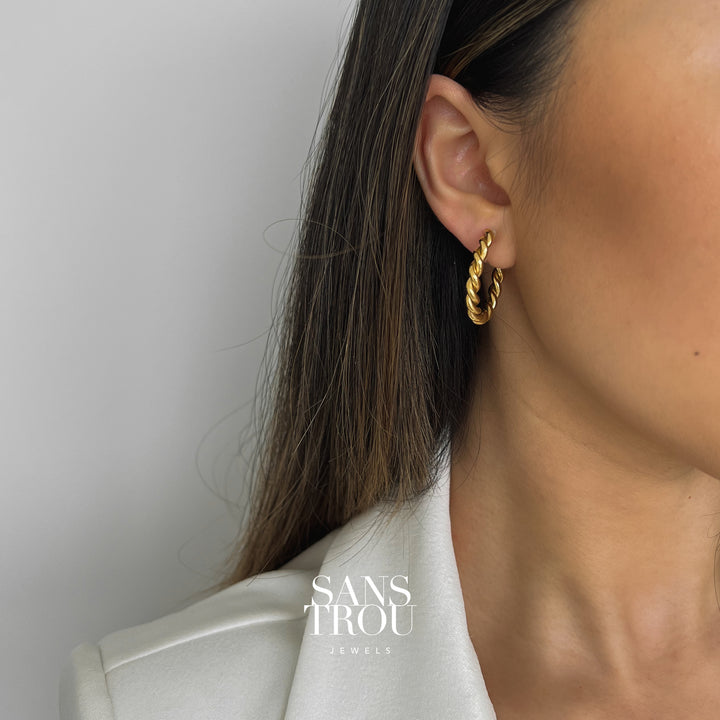 Model wears a twisted 18k gold plated clip-on hoop earring on the lobe. 