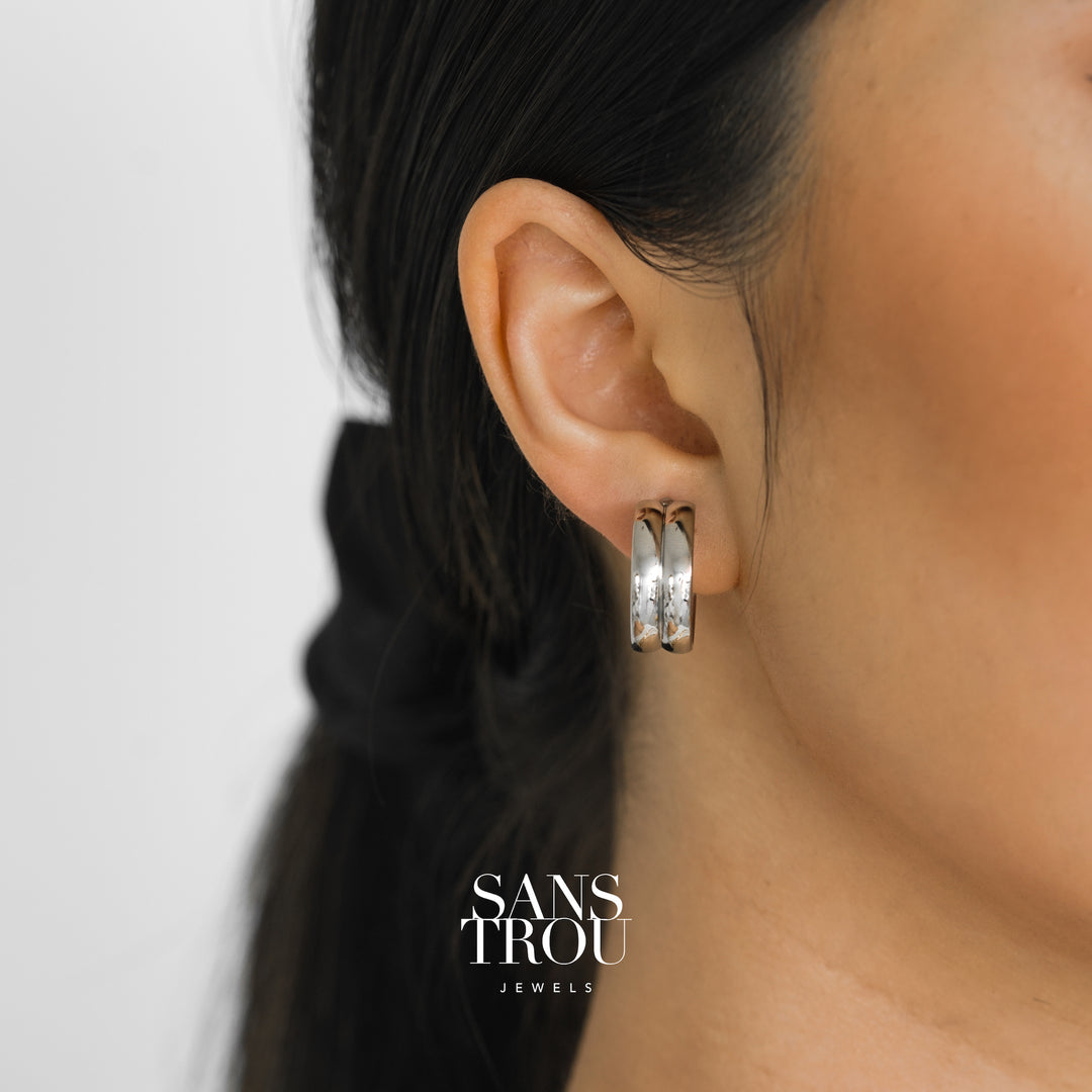 Model wears stainless steel silver clip-on hoop earring featuring a double banded hoop. 