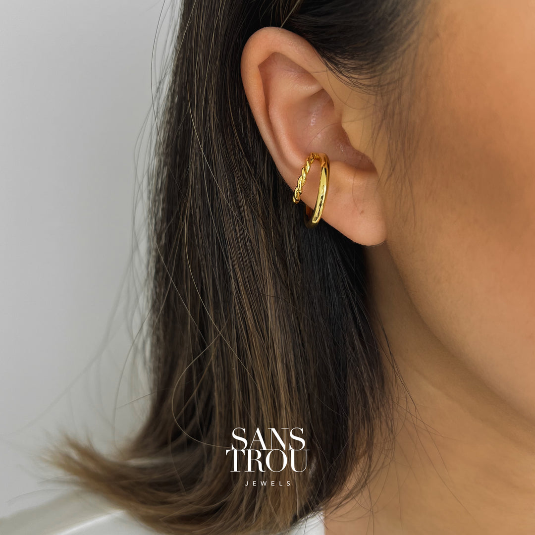 Model wears a gold double layered ear cuff on the conch. The twisted smaller rim stacks on top of the larger rim for a layered look. 