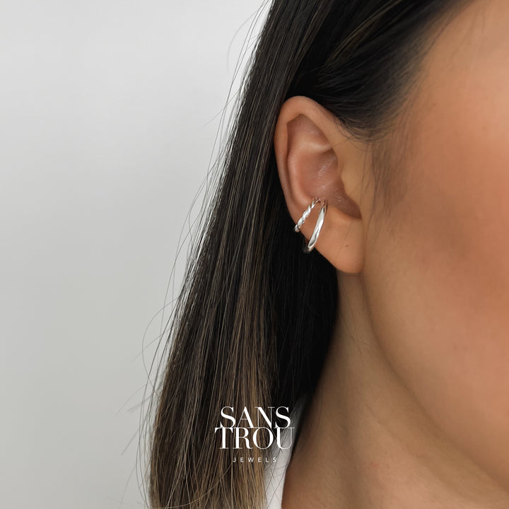 Model wears a silver double layered ear cuff on the conch. The twisted smaller rim stacks on top of the larger rim for a layered look. 