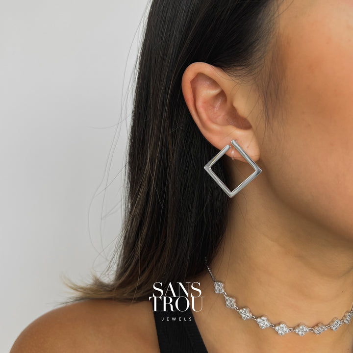 Model wears a stainless steel silver square clip-on earring on the lobe.